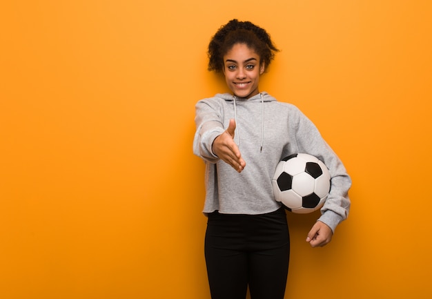 Giovane donna di colore di forma fisica che raggiunge fuori per accogliere qualcuno. In possesso di un pallone da calcio.