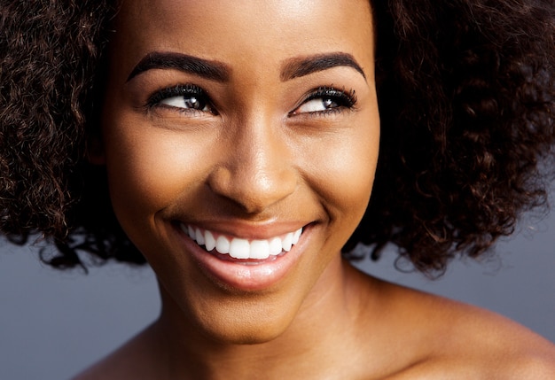 Giovane donna di colore sorridente con capelli ricci che osserva via
