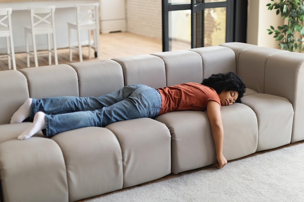 Giovane donna di colore stanca che dorme sul divano durante il giorno sentendosi esausta