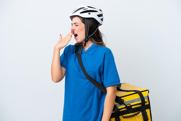 Giovane donna di consegna con zaino termico isolato su sfondo bianco che sbadiglia e copre la bocca spalancata con la mano