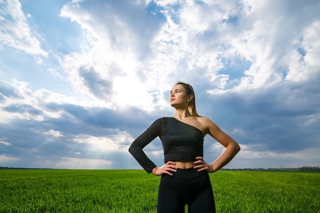 Giovane donna di corporatura atletica con un top nero e leggings neri su uno sfondo di cielo blu. Stile di vita sano, ragazza bruna atletica. Il concetto e la motivazione dello sport