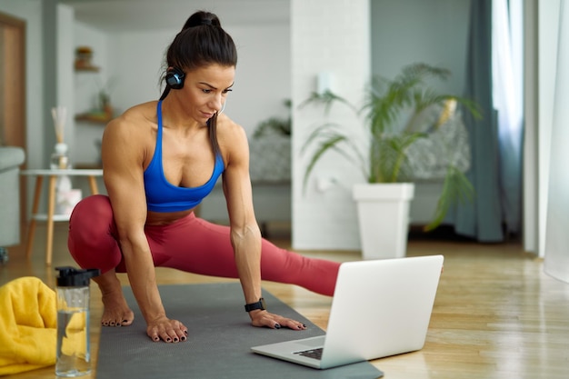 Giovane donna di corporatura muscolare che fa esercizi di stretching mentre utilizza il laptop a casa