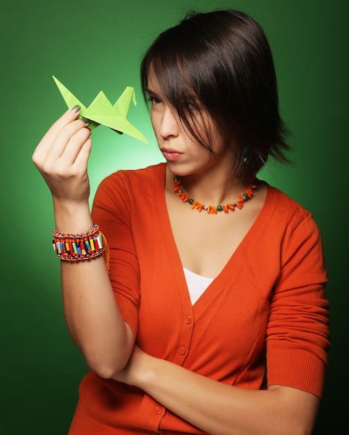 Giovane donna di espressione con uccello di carta su sfondo verde green