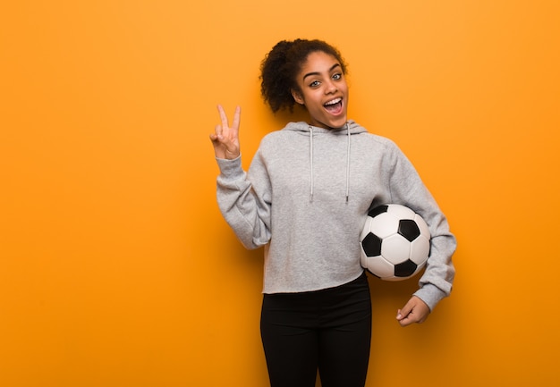 Giovane donna di forma fisica che fa un gesto della vittoria. In possesso di un pallone da calcio.