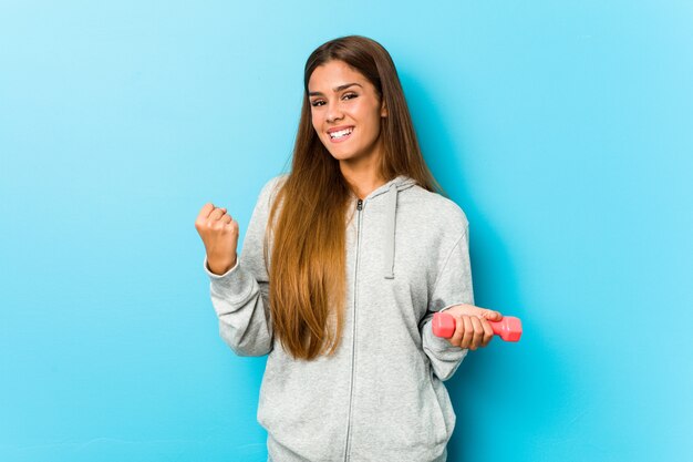 Giovane donna di forma fisica che tiene un peso incoraggiante spensierato ed eccitato. Concetto di vittoria.