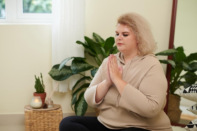 Giovane donna di grandi dimensioni seduta nella posizione del loto e tenendo le mani nel gesto di mudra durante la meditazione