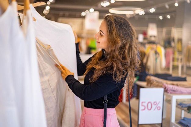 Giovane donna di lusso che sceglie vestiti a sconti stagionali godendosi lo shopping nella boutique di moda