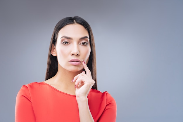 Giovane donna di modello con il vestito rosso che posa sul muro grigio