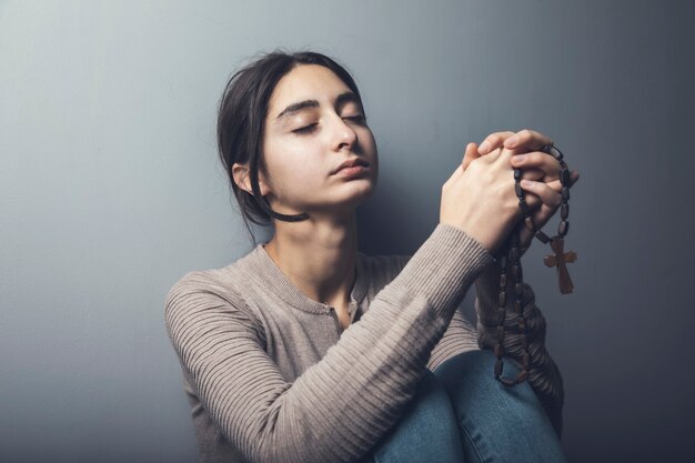 Giovane donna di preghiera che tiene croce di legno