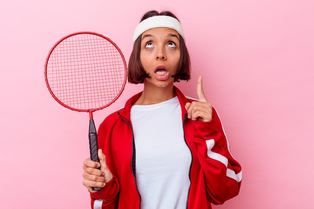 Giovane donna di razza mista che gioca a badminton isolato sul muro rosa rivolto verso l'alto con la bocca aperta.