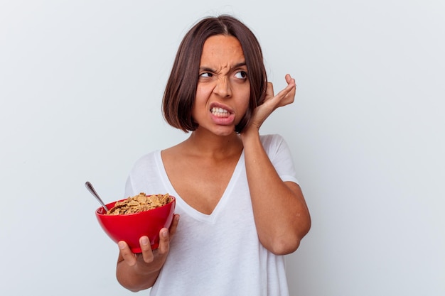 Giovane donna di razza mista che mangia cereali isolati sulle orecchie del rivestimento murale bianco con le mani.