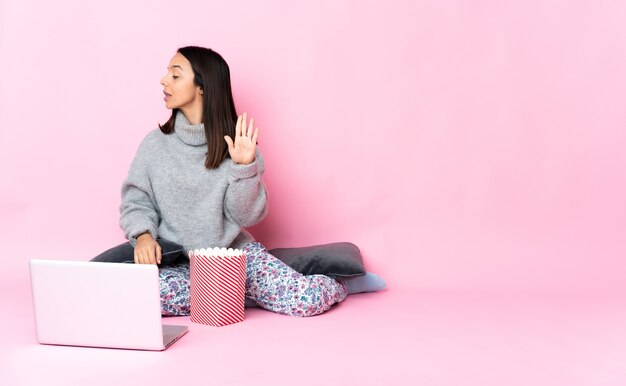 Giovane donna di razza mista che mangia popcorn mentre si guarda un film sul computer portatile