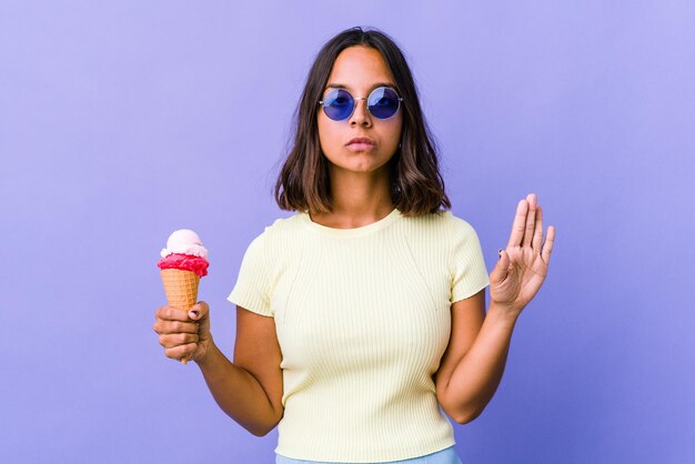 Giovane donna di razza mista che mangia un gelato in piedi con la mano tesa che mostra il segnale di stop, impedendoti.