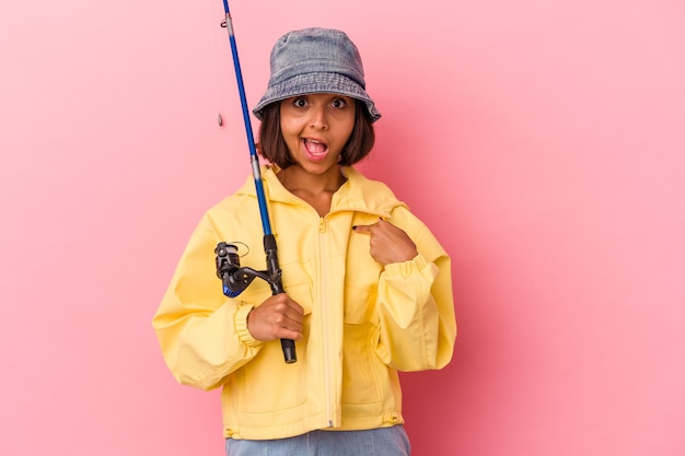 Giovane donna di razza mista che pratica la pesca isolata su sfondo rosa persona che punta a mano a uno spazio copia camicia, orgogliosa e fiduciosa