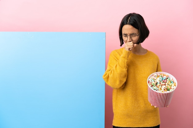 Giovane donna di razza mista che tiene i popcorn con un grande striscione su sfondo isolato che tossisce molto