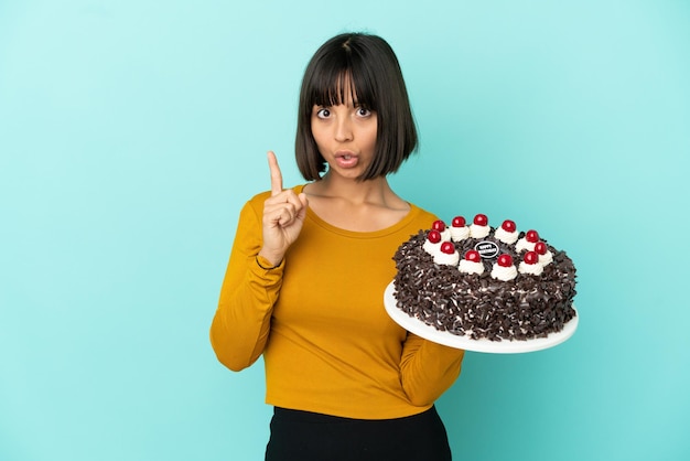 Giovane donna di razza mista che tiene in mano una torta di compleanno con l'intenzione di realizzare la soluzione mentre alza un dito