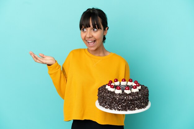 Giovane donna di razza mista che tiene la torta di compleanno con espressione facciale a sorpresa