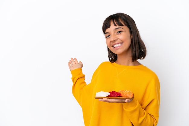 Giovane donna di razza mista che tiene sashimi isolato su sfondo bianco che allunga le mani di lato per invitare a venire