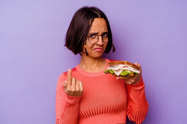 Giovane donna di razza mista che tiene un panino isolato su sfondo viola che punta il dito contro di te come se invitando ad avvicinarsi.