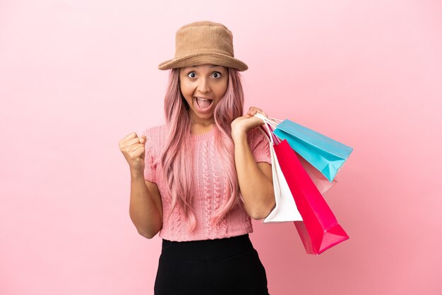 Giovane donna di razza mista con borsa della spesa isolata su sfondo rosa che celebra una vittoria nella posizione del vincitore