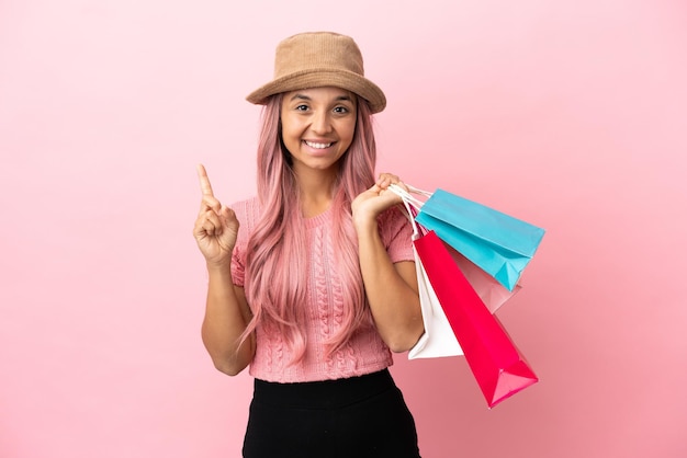 Giovane donna di razza mista con borsa della spesa isolata su sfondo rosa che mostra e solleva un dito in segno del meglio