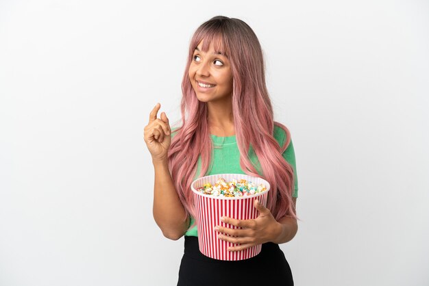 Giovane donna di razza mista con i capelli rosa che mangia popcorn isolato su sfondo bianco che indica una grande idea