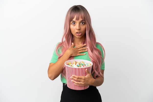 Giovane donna di razza mista con i capelli rosa che mangia popcorn isolato su sfondo bianco sorpresa e scioccata mentre guarda a destra