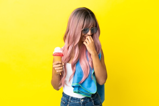 Giovane donna di razza mista con i capelli rosa che tiene il gelato isolato su sfondo giallo con dubbi