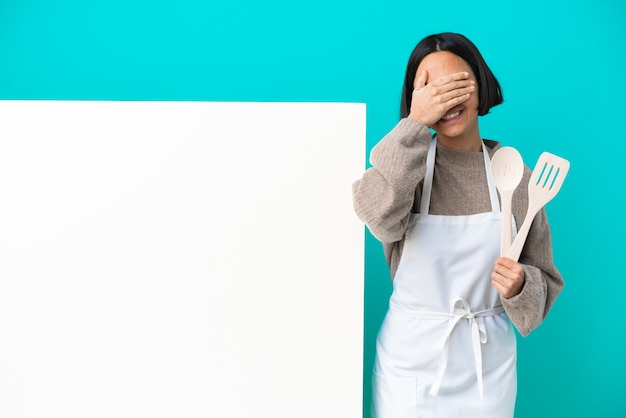 Giovane donna di razza mista cuoco con un grande cartello isolato su sfondo blu che copre gli occhi con le mani