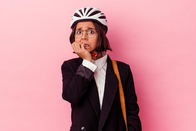 Giovane donna di razza mista d'affari che indossa un casco da bici isolato su sfondo rosa che si morde le unghie, nervosa e molto ansiosa.