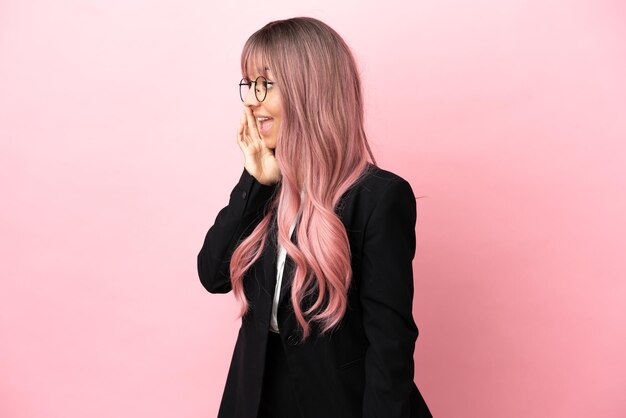 Giovane donna di razza mista d'affari con i capelli rosa isolata su sfondo rosa che grida con la bocca spalancata al laterale