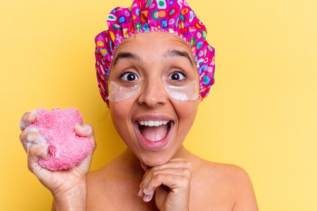 Giovane donna di razza mista fare il bagno tenendo una spugna con una benda sotto gli occhi