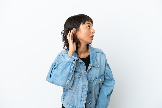 Giovane donna di razza mista isolata su sfondo bianco ascoltando qualcosa mettendo la mano sull'orecchio