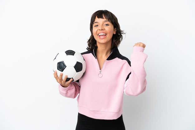 Giovane donna di razza mista isolata su sfondo bianco con pallone da calcio che celebra una vittoria