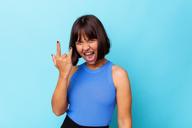 Giovane donna di razza mista isolata su sfondo blu che mostra gesto rock con le dita