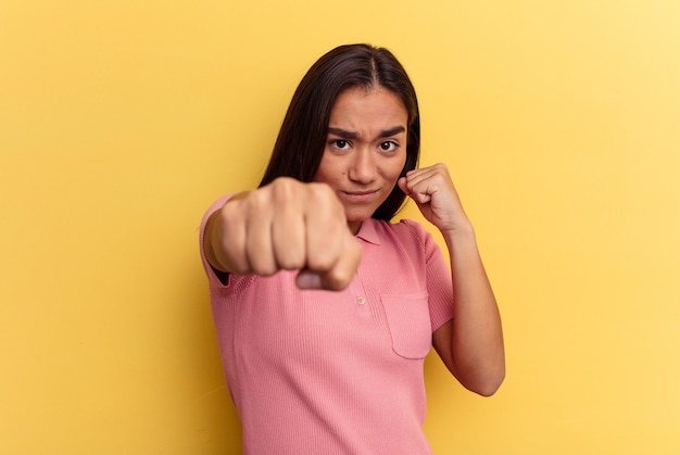 Giovane donna di razza mista isolata su sfondo giallo che lancia un pugno, rabbia, combattimento a causa di una discussione, boxe.