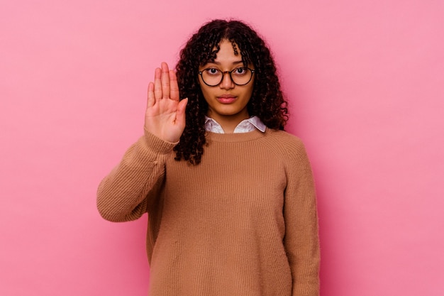 Giovane donna di razza mista isolata su sfondo rosa in piedi con la mano tesa che mostra il segnale di stop, impedendoti.