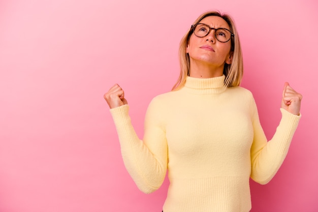 Giovane donna di razza mista isolata sul pugno di sollevamento rosa dopo una vittoria, concetto di vincitore.