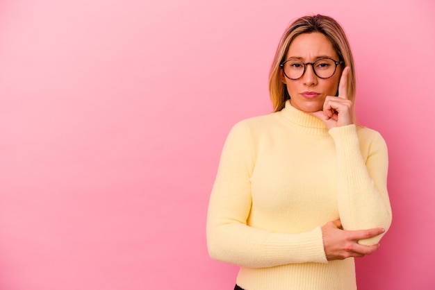 Giovane donna di razza mista isolata sul rosa che mostra il numero uno con il dito.