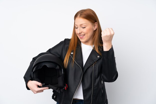 Giovane donna di redhead con un casco del motociclo sopra la parete bianca isolata che celebra una vittoria