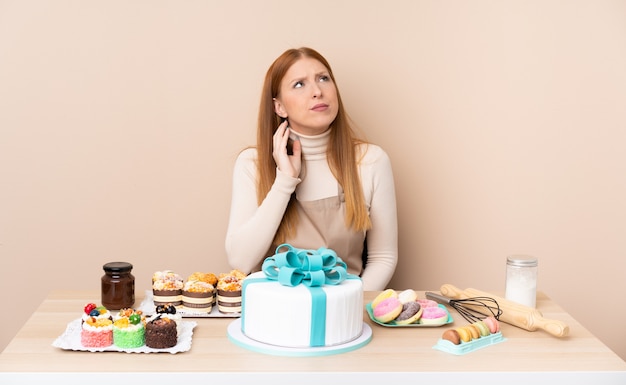 Giovane donna di redhead con una grande torta che pensa un'idea