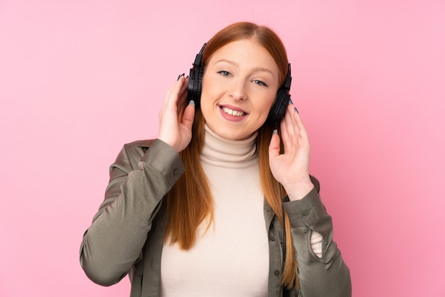 Giovane donna di redhead sopra musica d'ascolto isolata della parete rosa