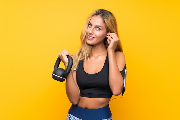 Giovane donna di sport che fa sollevamento pesi con kettlebell sopra giallo isolato