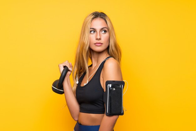 Giovane donna di sport che fa sollevamento pesi con kettlebell sopra la parete gialla isolata