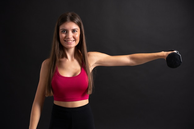 Giovane donna di sport che fa sollevamento pesi sopra fondo nero isolato