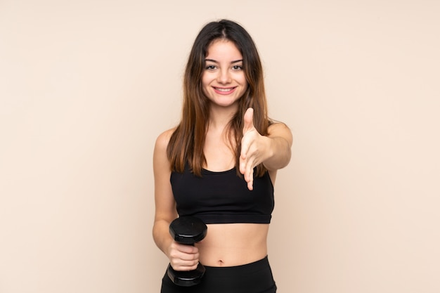 Giovane donna di sport che fa sollevamento pesi sulla stretta di mano beige della parete dopo il buon affare