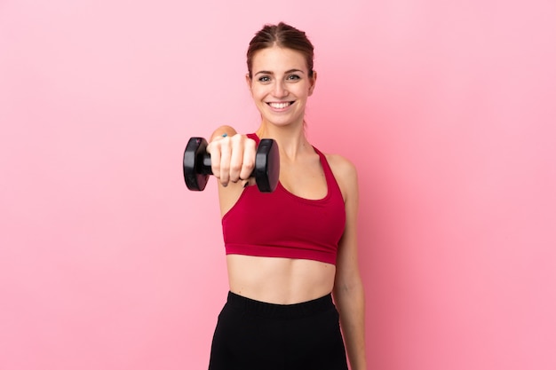 Giovane donna di sport sopra la parete rosa isolata che fa sollevamento pesi