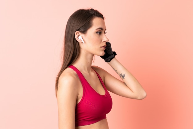 Giovane donna di sport sopra musica d'ascolto isolata della parete rosa