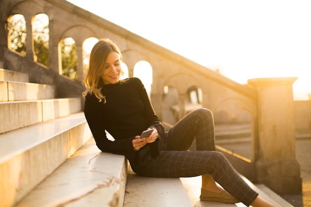 Giovane donna di Trendu con il telefono cellulare che si siede alle scale all&#39;aperto