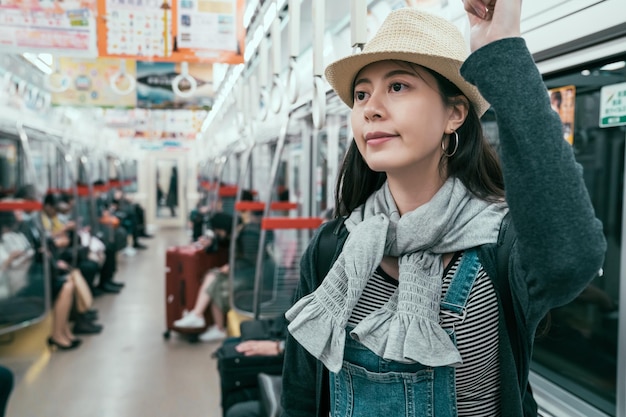 Giovane donna di viaggio che tiene la maniglia mentre ci si sposta nel tram moderno. Passeggero felice che si gode il viaggio con i mezzi pubblici. ragazza sorridente zaino in spalla che torna in hotel prendendo la metropolitana a osaka in giappone.